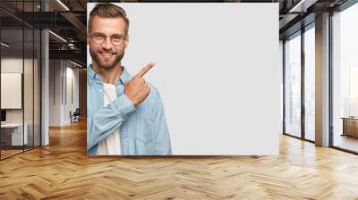 This idea just fascinated me. Attractive young unshaven individual with happy expression, indicates with index finger at blank copy space, advertises you place to vist, isolated over white wall Wall mural