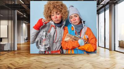 Upset women feel tired after camping hold wood and lantern look sadly at camera have active rest in forest have frozen face after being outdoors on cold winter weather drssed in warm clothes Wall mural