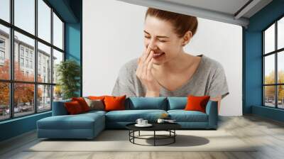 Vivacious teenage girl giglling with her eyes screwed up in a moment of fun as she sitting against white studio wall. Happy natural laughing young casual female covering mouth. Human face expressions Wall mural