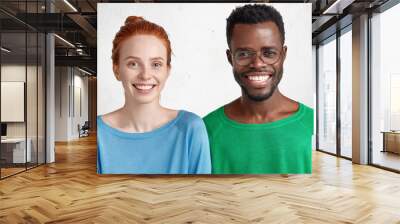 Waist up portrait of mixed race couple with warm broad smiles happy to spend time together. Attractive red haired freckled female and her best dark skinned male demonstrate interracial friendship Wall mural