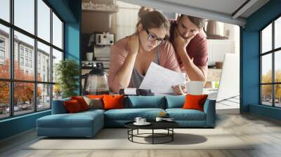 Young Caucasian family having debt problems, not able to pay out their loan. Female in glasses and brunette man studying paper form bank while managing domestic budget together in kitchen interior Wall mural