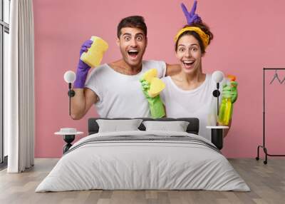 young male and female playing fools while standing against white pink wall resting after doing clean Wall mural