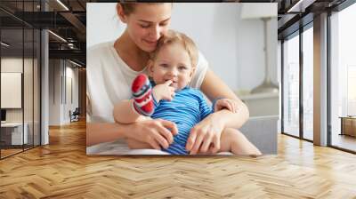 Young mother with her one years old little son are helps son to take the first steps in the bedroom at the weekend together.  Selective focus. Casual lifestyle photo series in real life interior Wall mural