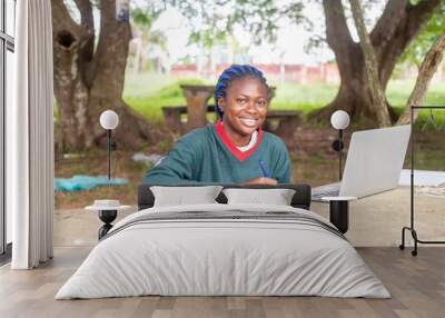 young female freelancer writing blog post using laptop sitting a a park with tress Wall mural