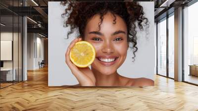  a smiling woman with curly hair holding a half-eaten lemon wedge. Wall mural