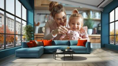 Caring young mother teaching small preschool kid daughter saving money or planning future purchases, putting coins in small piggybank in modern kitchen Wall mural