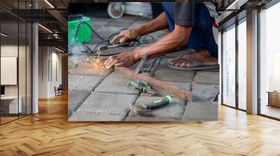 Person welding metal on paved surface with tools scattered Wall mural