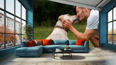 Friendship and love of man and dog. Happy young man kissing with his friend - dog Labrador Wall mural