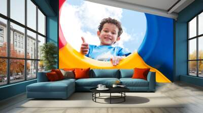 kid boy thumbs up and having fun to play on children's climbing toy at school playground,back to school activity,looking up view Wall mural