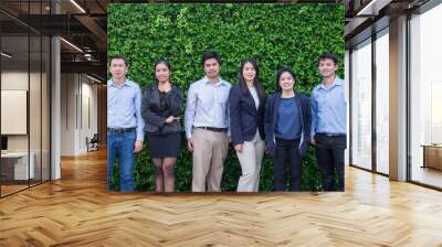 Team of Asian business man and woman looking at camera with smiling face outside office at green leaf wall. Wall mural