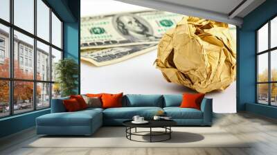 Crumpled gold paper ball on a white background with dollar bills, representing waste and financial concepts. Wall mural