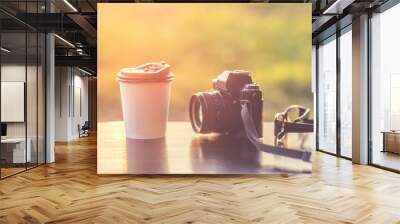 Coffee mugs plastic and classic camera models on a wooden table against sunlight and a blurred background. Wall mural