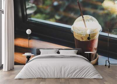 Side view of iced dark cold brew americano coffee on the plastic cup and brown plastic straw on the wooden bar table with copy space in coffee shop. Wall mural