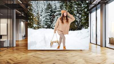 Happy woman with sledge walking among winter forest Wall mural