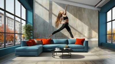 Modern jazz dancer with long hair young girl wearing black costume or woman passionately dancing on grey sunlit studio or dancing room background flying to the sky Wall mural