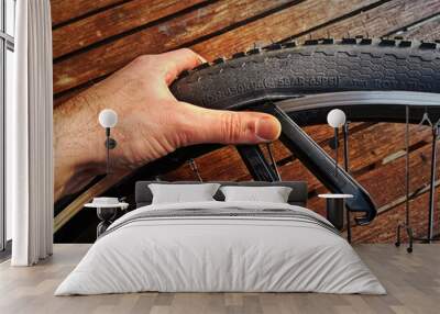 A hand manipulating a bicycle tire for mending, maintenance and repair of a flat mountain bike tube with tire iron tools. Wooden workbench in the background. Wall mural