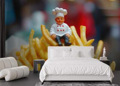 A small chef figurine dressed in white sits atop a large serving of golden french fries, capturing a whimsical miniature scene of culinary delight and playful imagination. Wall mural