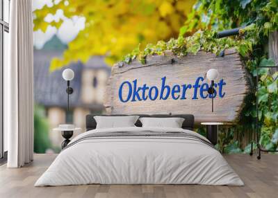 An Oktoberfest sign crafted from weathered wood, surrounded by lush green leaves. This image captures the festival's celebratory atmosphere in a serene, rural setting. Wall mural