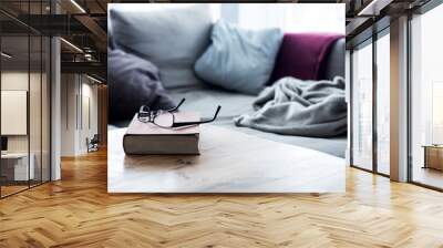 book with eyeglasses on wooden table in front of cozy couch Wall mural