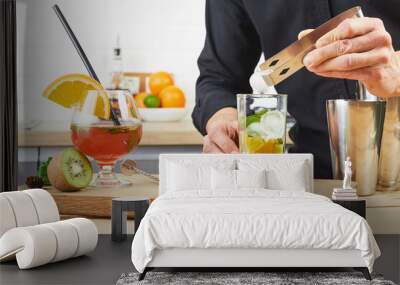 A man prepares a cocktail at a house party. An experienced bartender throws ice into a cocktail glass. Making cocktails at home in the kitchen. Wall mural