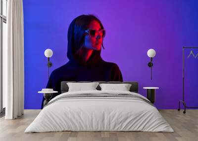 Girl with long hair and sunglasses in a white shirt poses in neon light in the studio. Wall mural