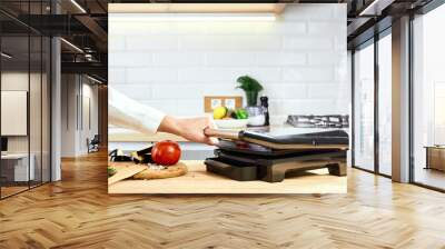 The woman's hands prepares vegetables on an electric grill on wooden table. Process of cooking vegetables on electric grill. Smoke in the home kitchen. Wall mural