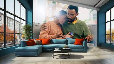 Sad, home and black couple with hug, conversation and emotions with discussion, grief and loss. People, apartment and man with woman, embrace or talking with reaction, crying and support with anxiety Wall mural