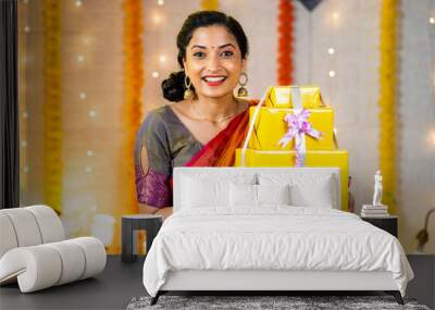 Cheerful excited young indian girl showing gift boxes for diwali festival celebration by looking at camera at home - concept of festival offers, surprise present and tradition. Wall mural