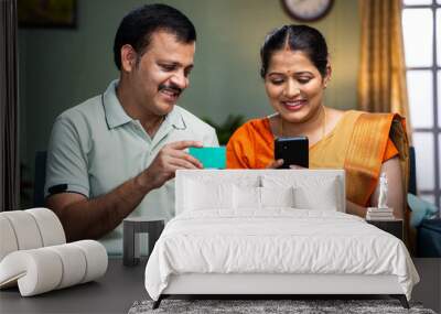 Happy middle aged couple making online payment using credit on mobile phone at home - concept of online shopping, secure transaction and banking or finance Wall mural