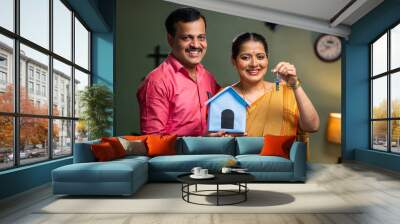 Happy smiling couple showing new house keys by toy home while looking camera - concept of new home purchasing, home loan and investment. Wall mural