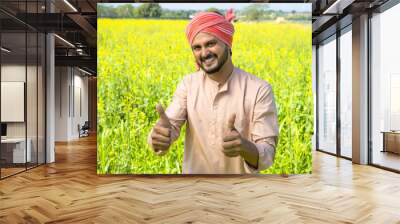 Happy smiling farmer showing thumbs up gesture by looking at camera at farmlad - concept of small agri business and rural Indian village lifestyle Wall mural