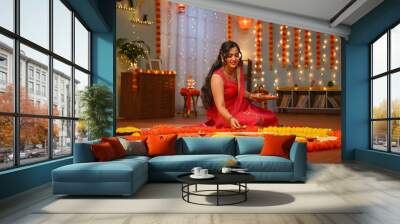 Happy young Indian woman placing diya lamps on decorated flower rangoli for diwali festival celebration at home - concept of festive preparation, traditional culture and spirituality Wall mural