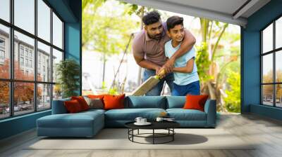 indian father teaching his son to playing cricket game at park - concept of Shared passion, family bonding and fatherhood Wall mural