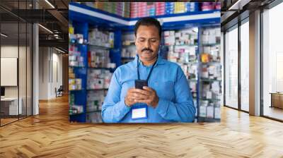 Pharmacist busy using mobile phone at retail pharma medical store - concept of relaxation, checking stock and small business. Wall mural