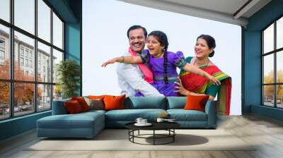 Playful excited indian girl kid while holding by father with mother near farmland - concept of parents support, family bonding and happiness Wall mural