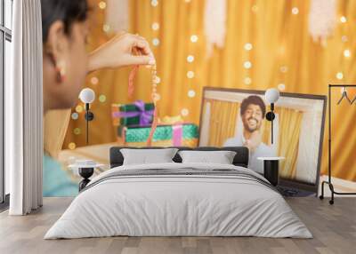 shoulder view of sister video calling her brother to tie rakhi or Raksha Bandhan during festival and showing gift received - Concept of far Rakshabandhan celebration by using technology and internet. Wall mural