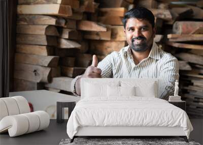 Smiling carpenter showing thumbs up by looking at camera while working at shop - concept of approve, promotion, artisan and wood working. Wall mural