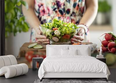 A view of a young woman's hands holding a glass bowl full of a healthy mixed salad Wall mural