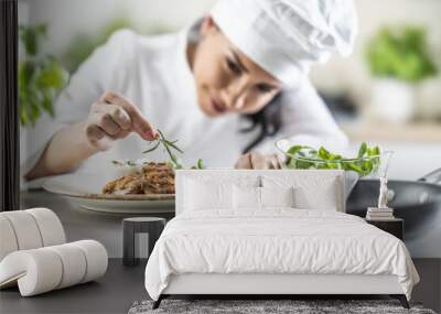 A young female chef finishes a meal with a sprig of rosemary in a restaurant kitchen Wall mural