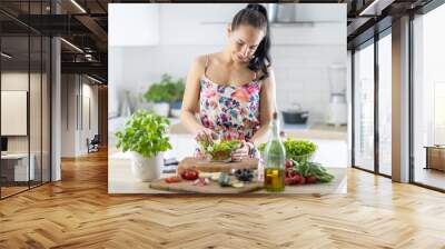 A young woman prepares a healthy lettuce salad from fresh ingredients Wall mural