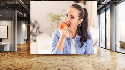 Beautiful brunette woman sitting in a living room biting off an apple Wall mural