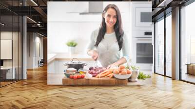 Cheerful young woman is happy to prepare lunch in her kitchen. She prepares food from meat and vegetables and other healthy ingredients Wall mural