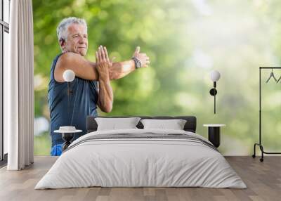 Elderly fit man stretches his arm on a summer day outdoors, wearing watches and earphones Wall mural