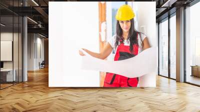 Female construction supervisor studies building plans in the red overall and yellow safety helmet Wall mural