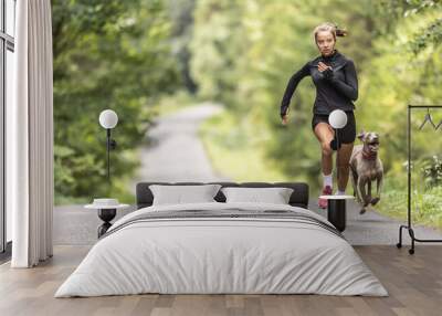 Female young sprinter runs fast up the hill followed by her dog Wall mural