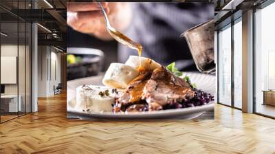 Food decorating hand of a chef pours sauce over hearty food of meat, dumplings and cabbage Wall mural