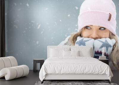 Girl warming her hands in gloves by breathing warm air on them Wall mural