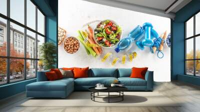 Healthy fresh salad with tomatoes surrounded with exercise equipment, carrtot celery and measuring tape - top of view Wall mural