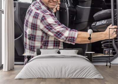 Mid-aged truck driver in checkered shirt and jeans enters the cab of his articulated truck Wall mural