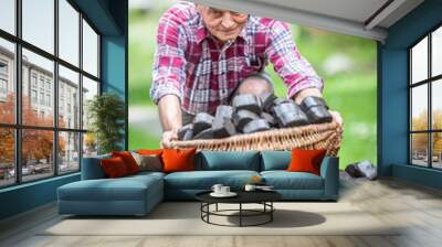 Portrait of an old man picking up a basket full of coal briquettes from a pile in the backyard Wall mural